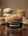 Cinnamon Bun Body Butter jar with icing, surrounded by cinnamon rolls, cookies, and lattes.