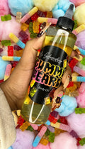 Hand holding Gummy Bears body oil bottle surrounded by gummy candies and cotton candy.