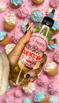 Hand holding Buttercream Frosted Cupcake body oil with cupcakes and sprinkles background
