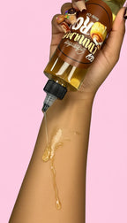 Woman applying cinnamon roll scented body oil to forearm on pink background