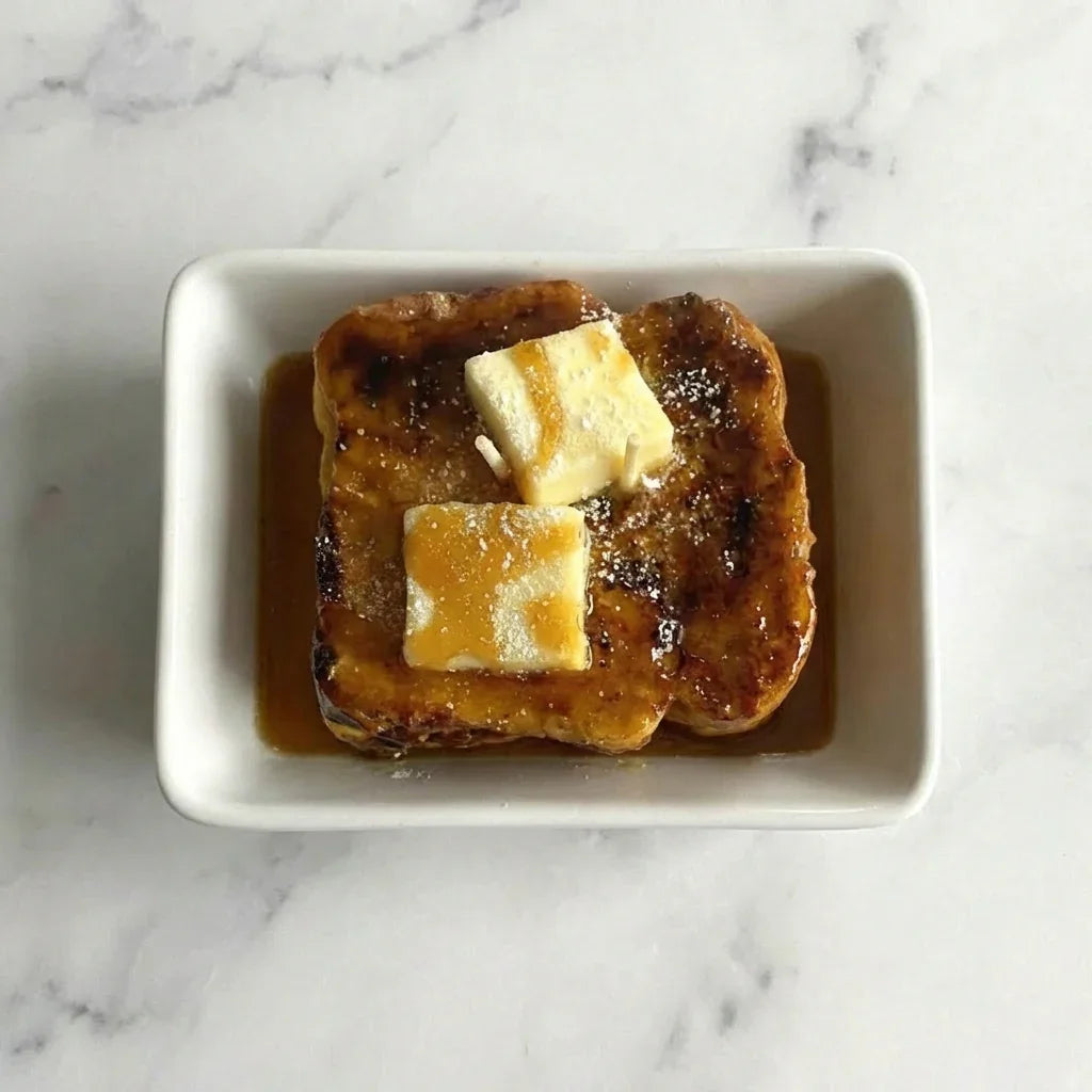 Aerial view of French toast with syrup and butter on a white dish, marble background