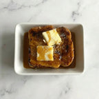 Aerial view of French toast with syrup and butter on a white dish, marble background