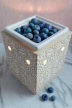 Blueberry-shaped wax melts in a decorative ceramic warmer on a marble surface