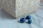 Realistic blueberry wax melts on marble beside a decorative cream and gold container