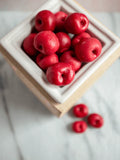 Red cherry-shaped wax melts in a white warmer on a marble surface